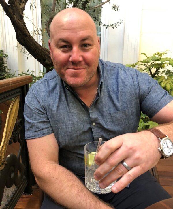 Photo of Matthew Barsamian sitting down and holding up a beverage in a glass